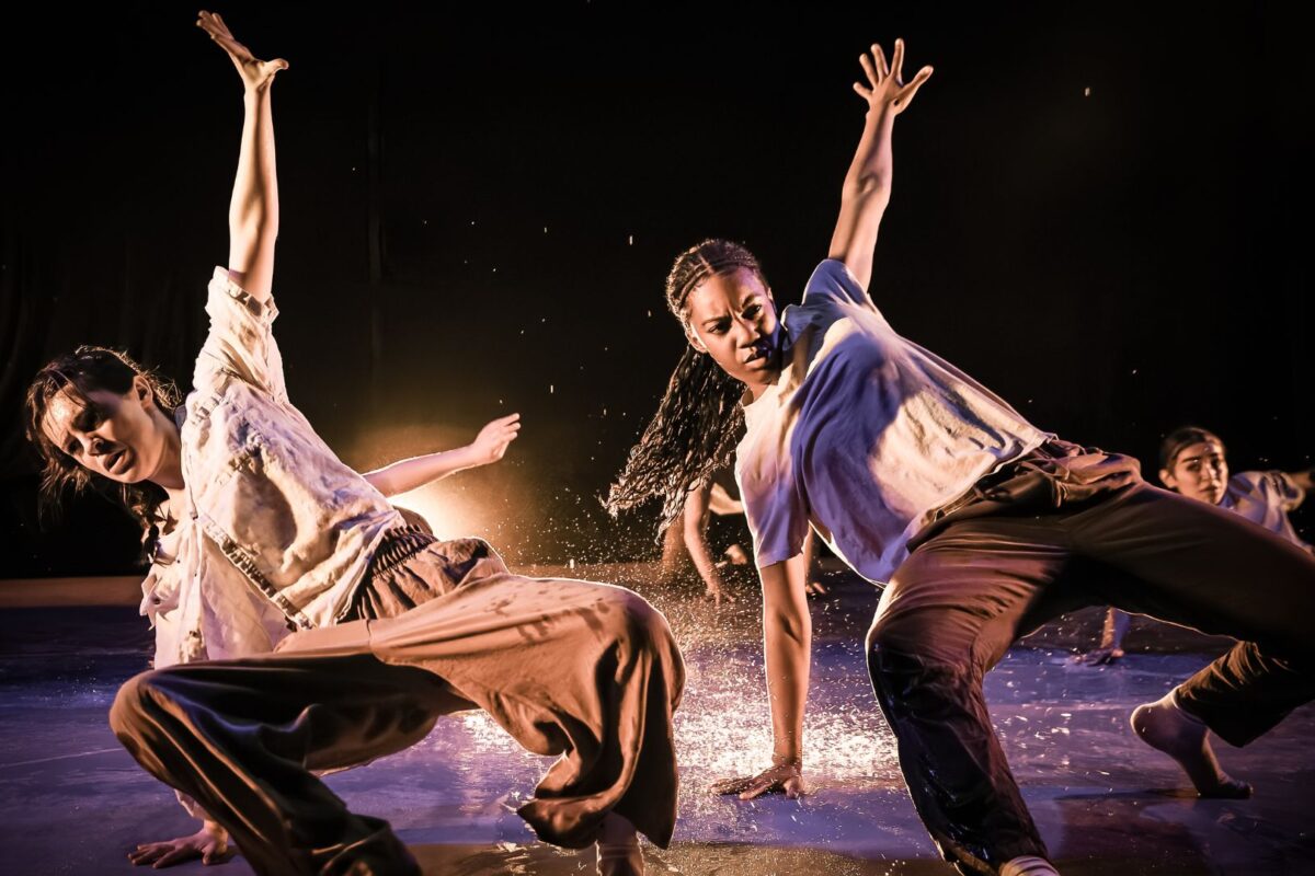 Two dancers crouched on the floor with their arms reaching towards the ceiling