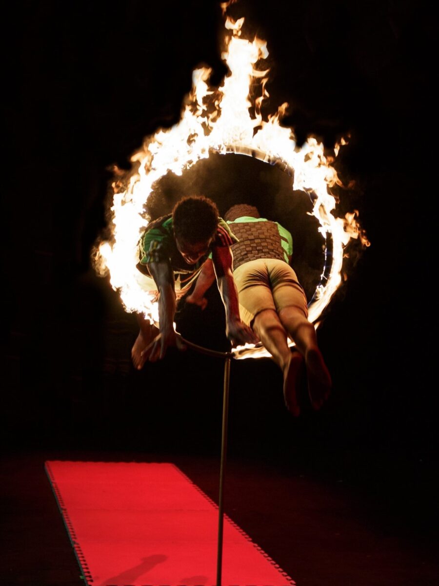 Two circus leap in opposite directions through a hoop which is on fire