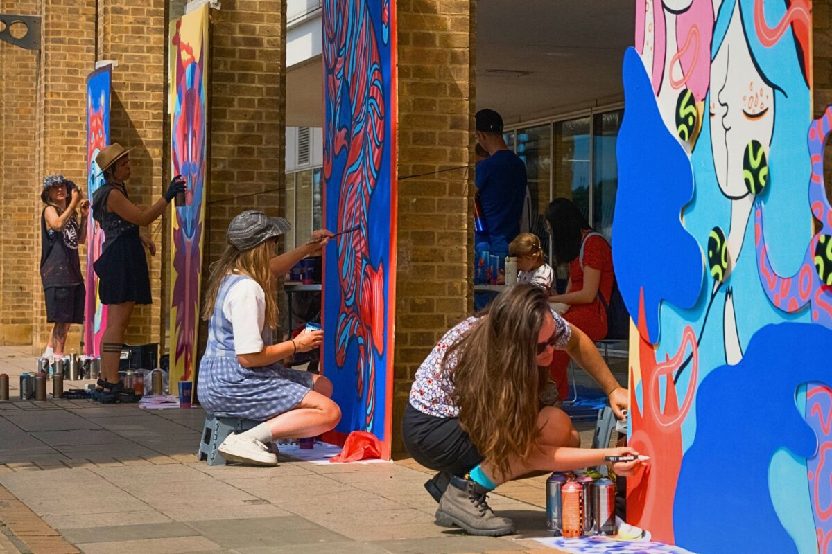 two artists crouch in front of large street art murals