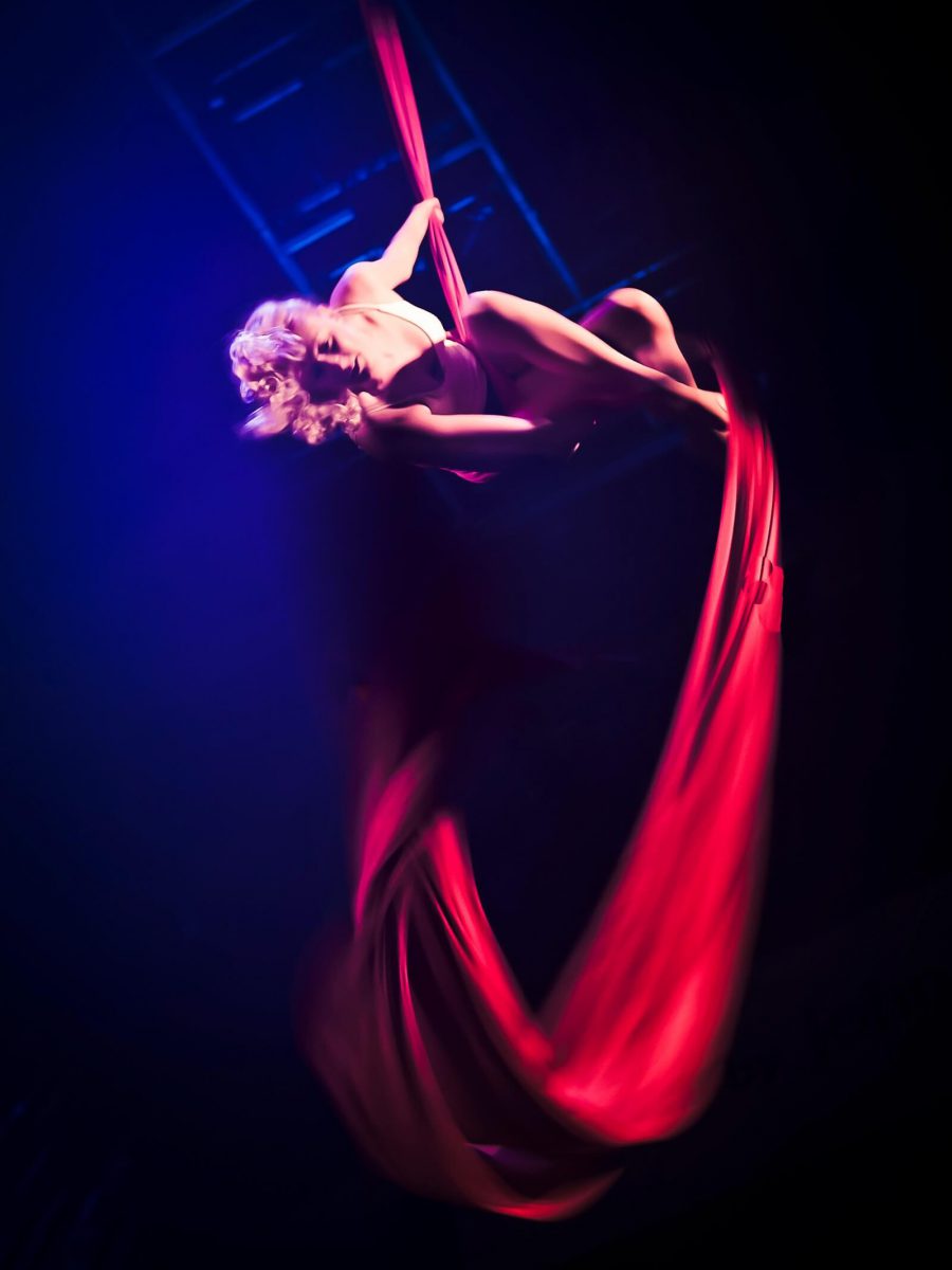 a circus performer hangs from red aerial silks