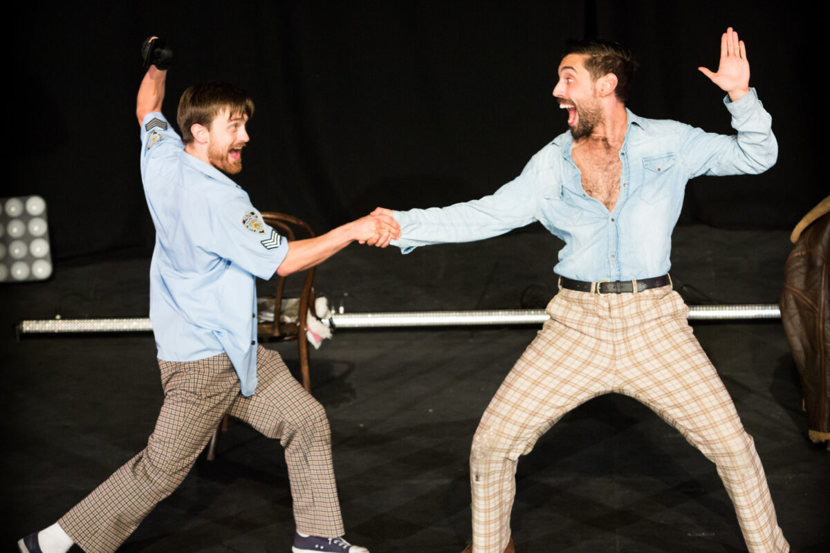 Two performers from Police Cops shake hands on stage in a dramatic fashion